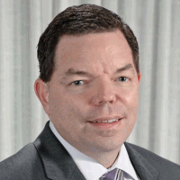 Man in a suit smiles at the camera against a light background.