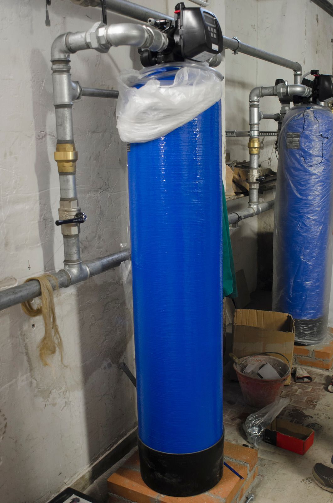 Blue water filtration tank with metal pipes and pump in a utility room.