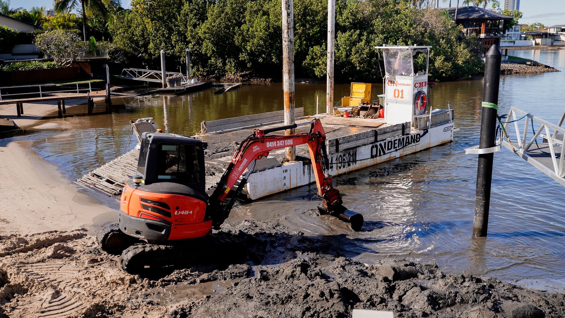 Excavator Works in Muddy Water Near a White Boat — On Demand Diggers and Demolitions in Molendinar, QLD