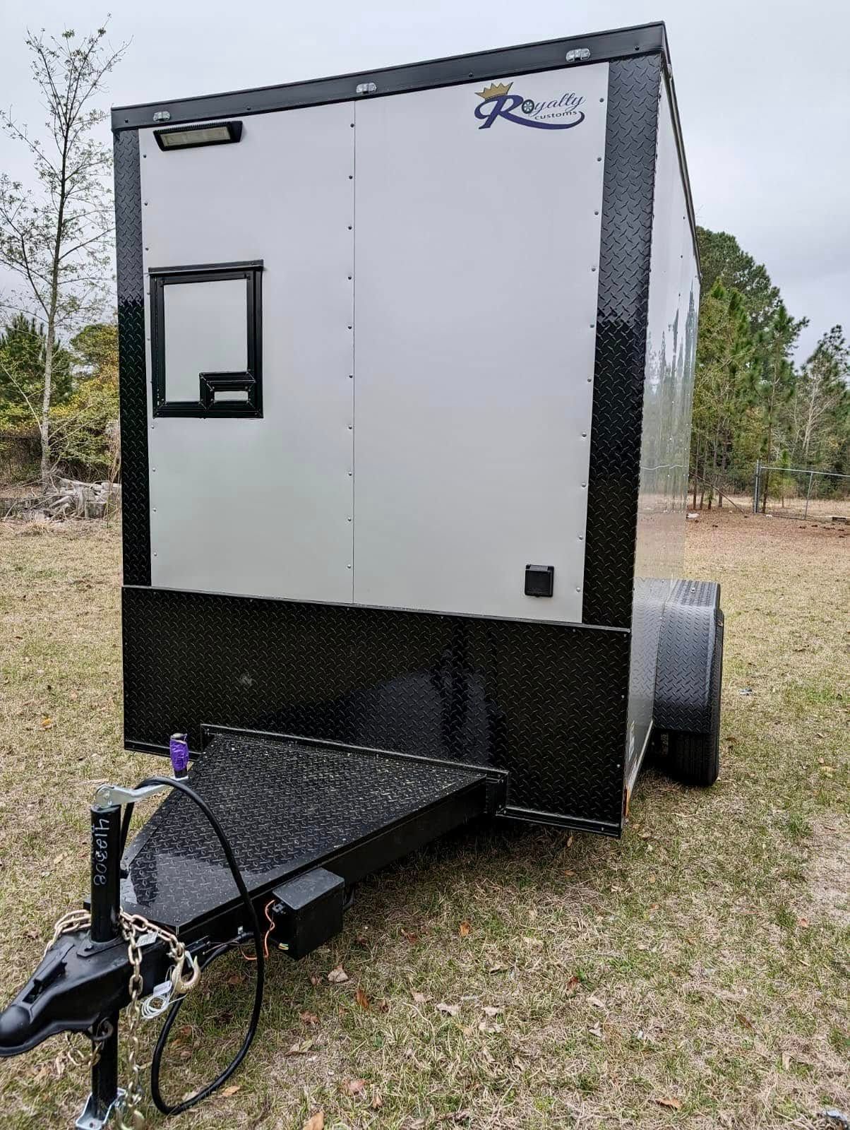 A black and white trailer is parked in a grassy field.