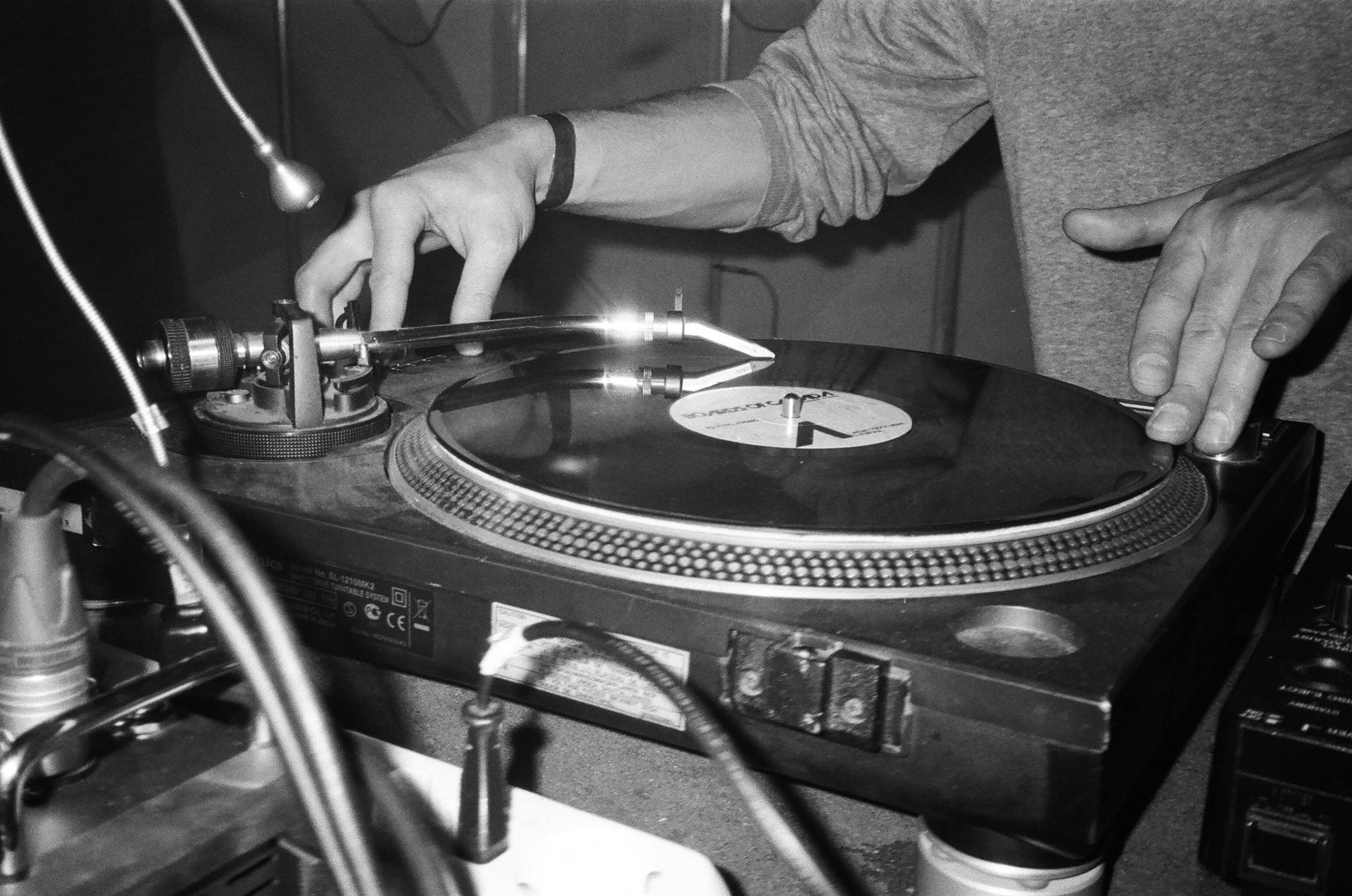 DJ's hands on turntable, spinning vinyl record, close-up, black and white.