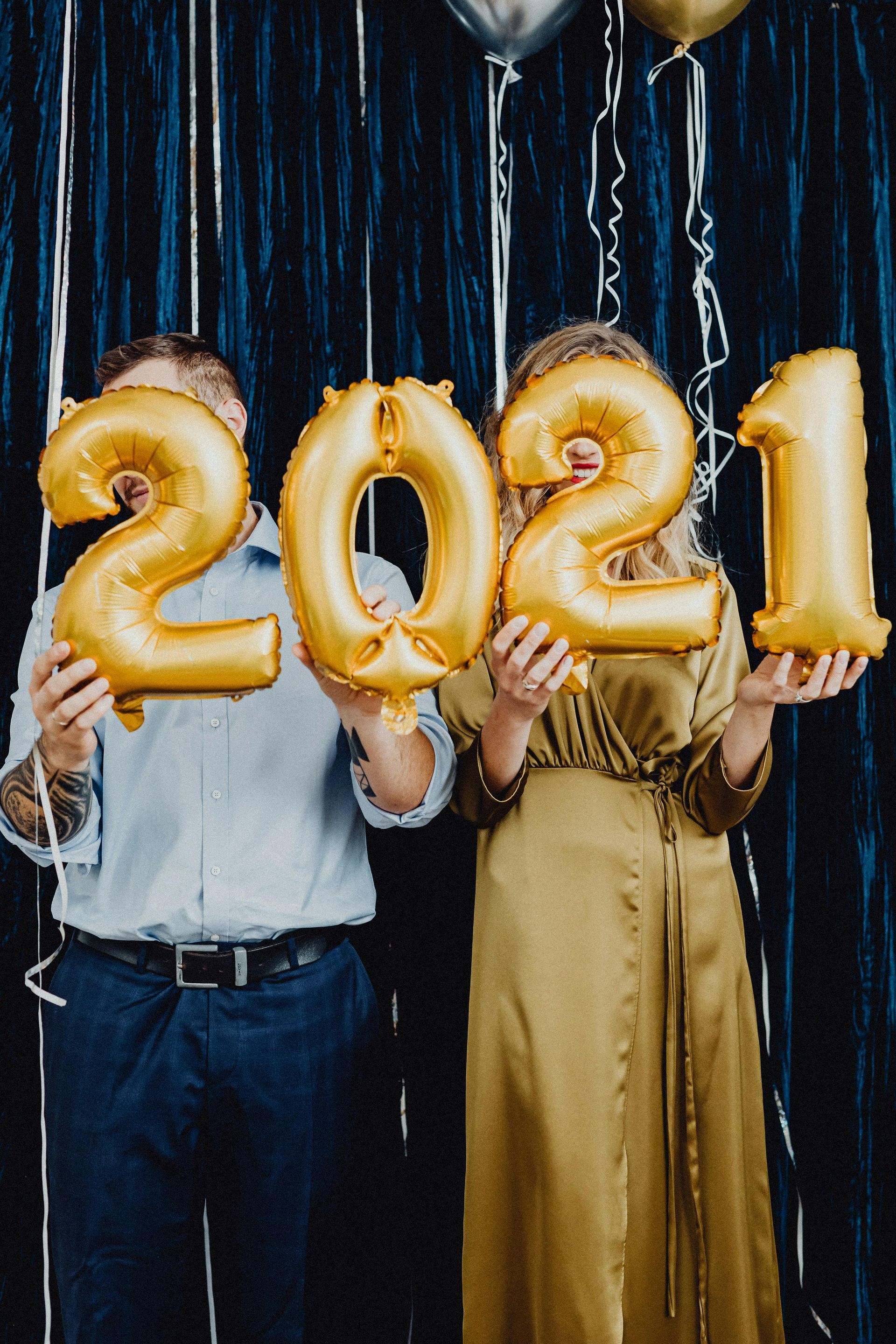 Two people hold gold balloon numbers forming