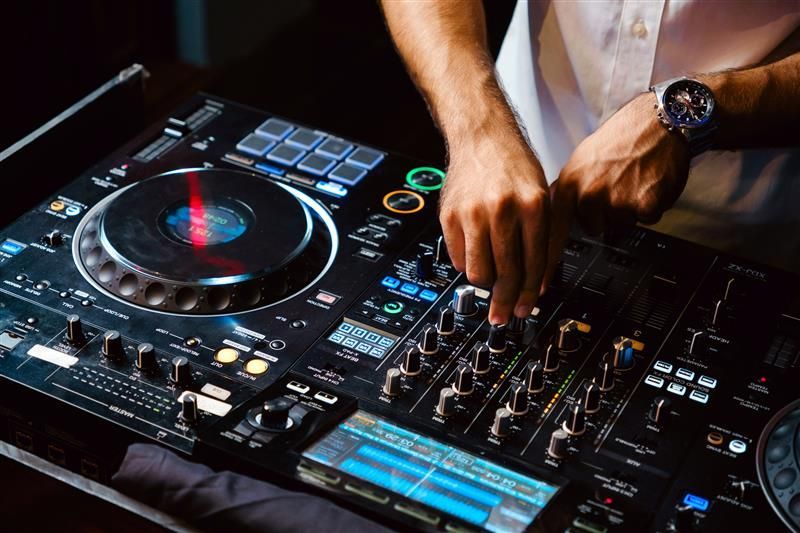 DJ using a black and silver sound mixing console at a dark club, focused on knobs and controls.