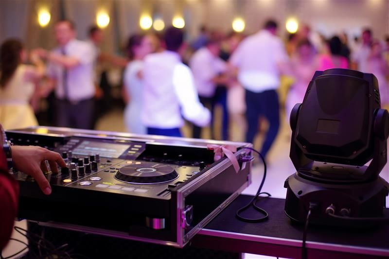 DJ mixing music at a party; people dance on a lit dance floor.