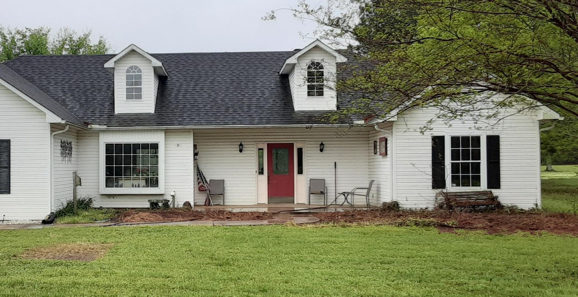 A white house with a red door and black shutters is sitting on top of a lush green field.