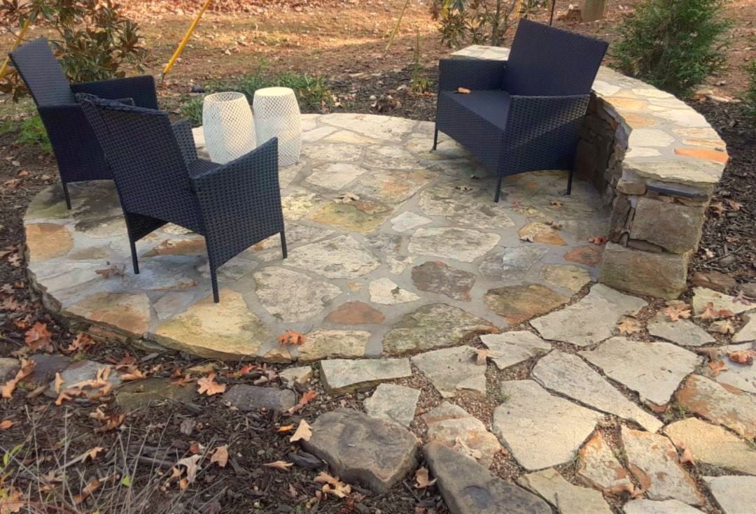 Stone patio with three black chairs and small stone retaining wall.