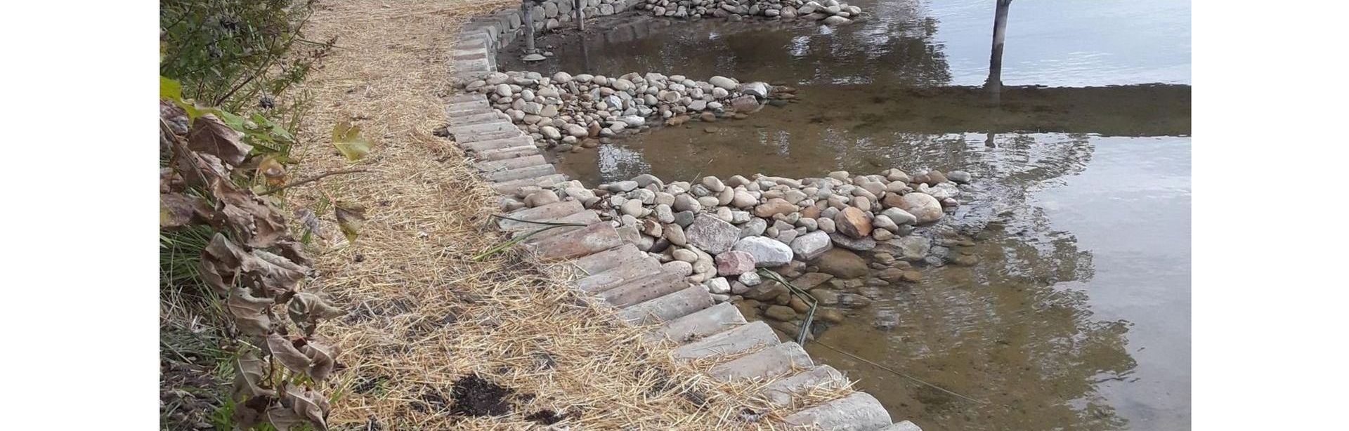 A rocky shoreline next to a body of water with a bridge in the background.