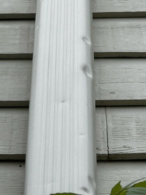 White gutter with dents against gray siding.