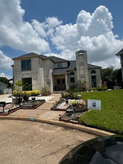 Two-story light brick house with lawn, landscaping, and a cloudy sky.