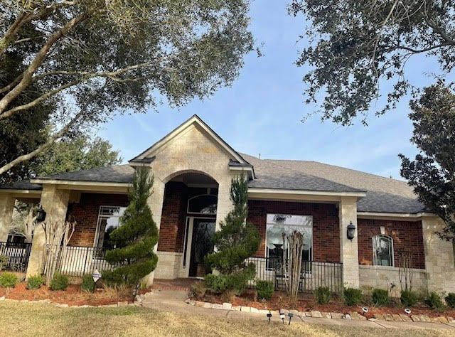 A brick home with arched entryway and manicured landscaping under a blue sky.