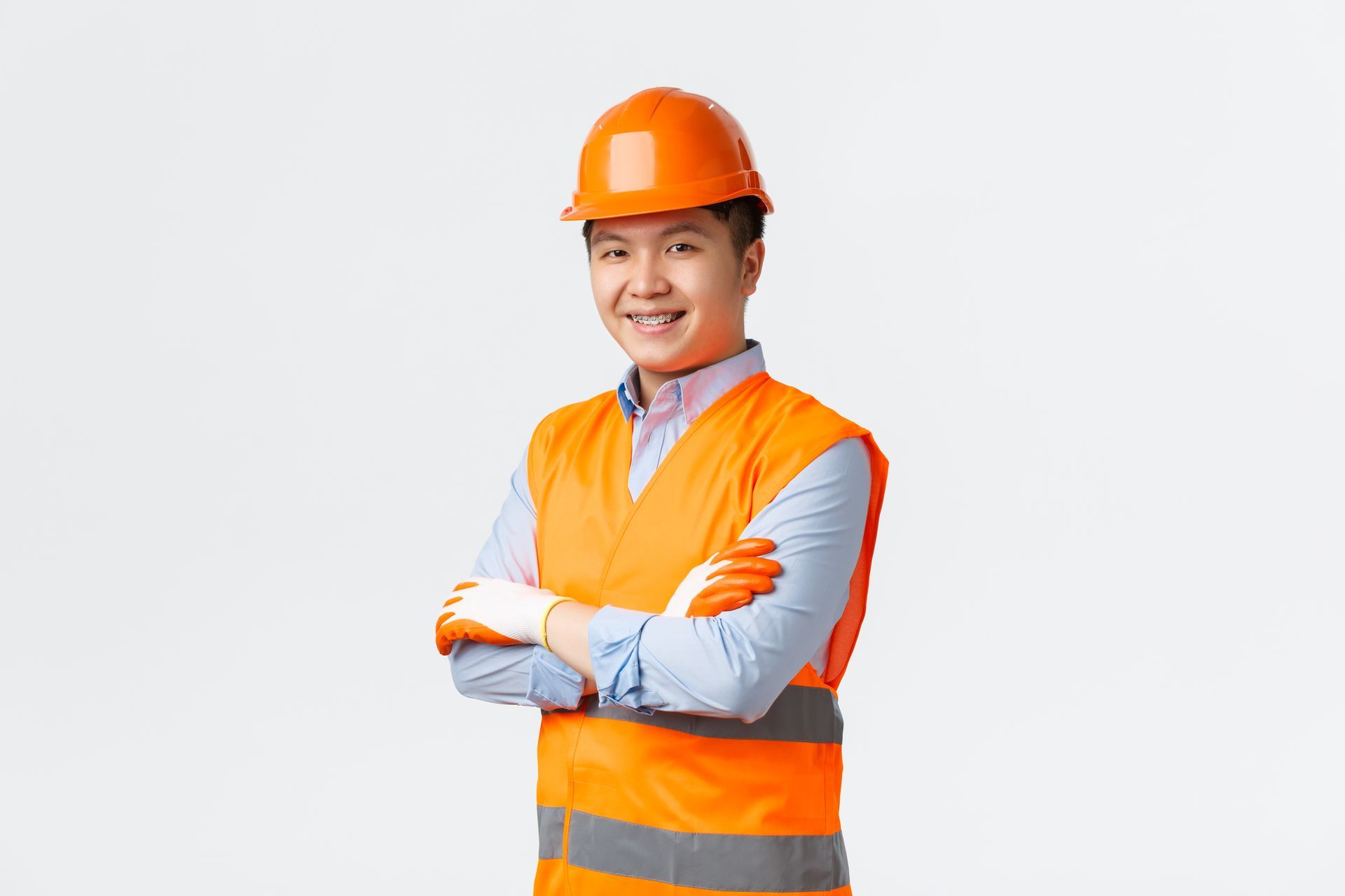 Person in orange safety gear, arms crossed, smiling, wearing a hard hat, and gloves.