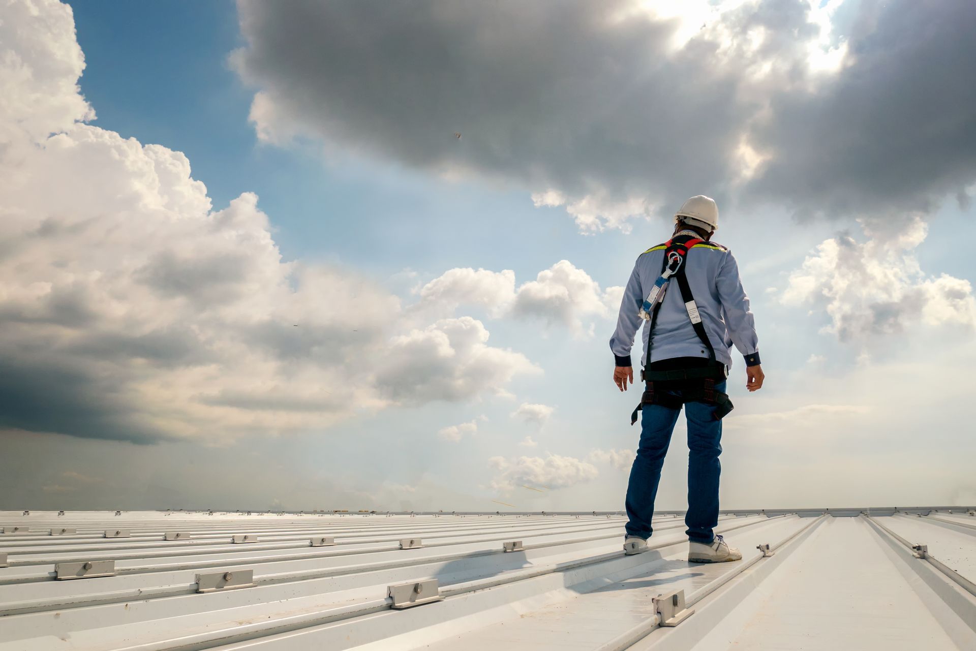 Person in safety harness on a rooftop, cloudy sky overhead.