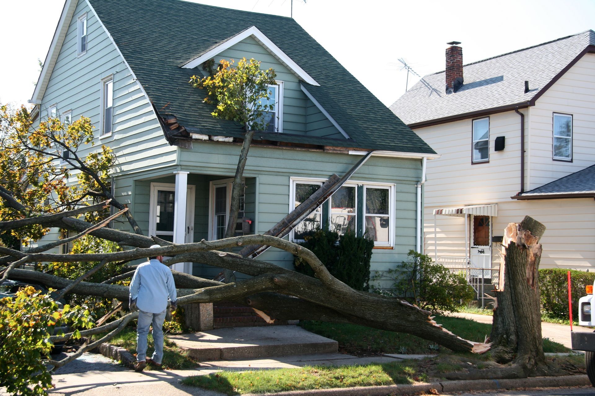 Tree fallen on house; man inspects damage to front porch and roof.