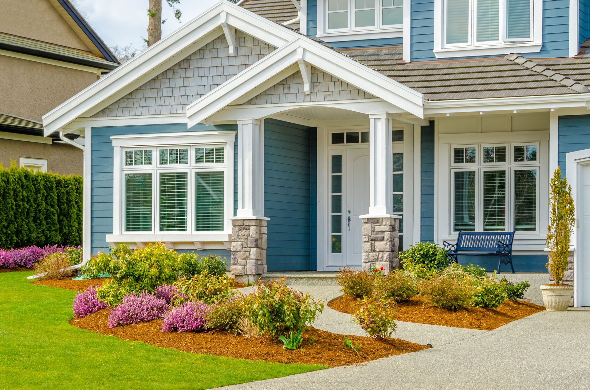 Blue house with white trim, porch, and landscaped yard.