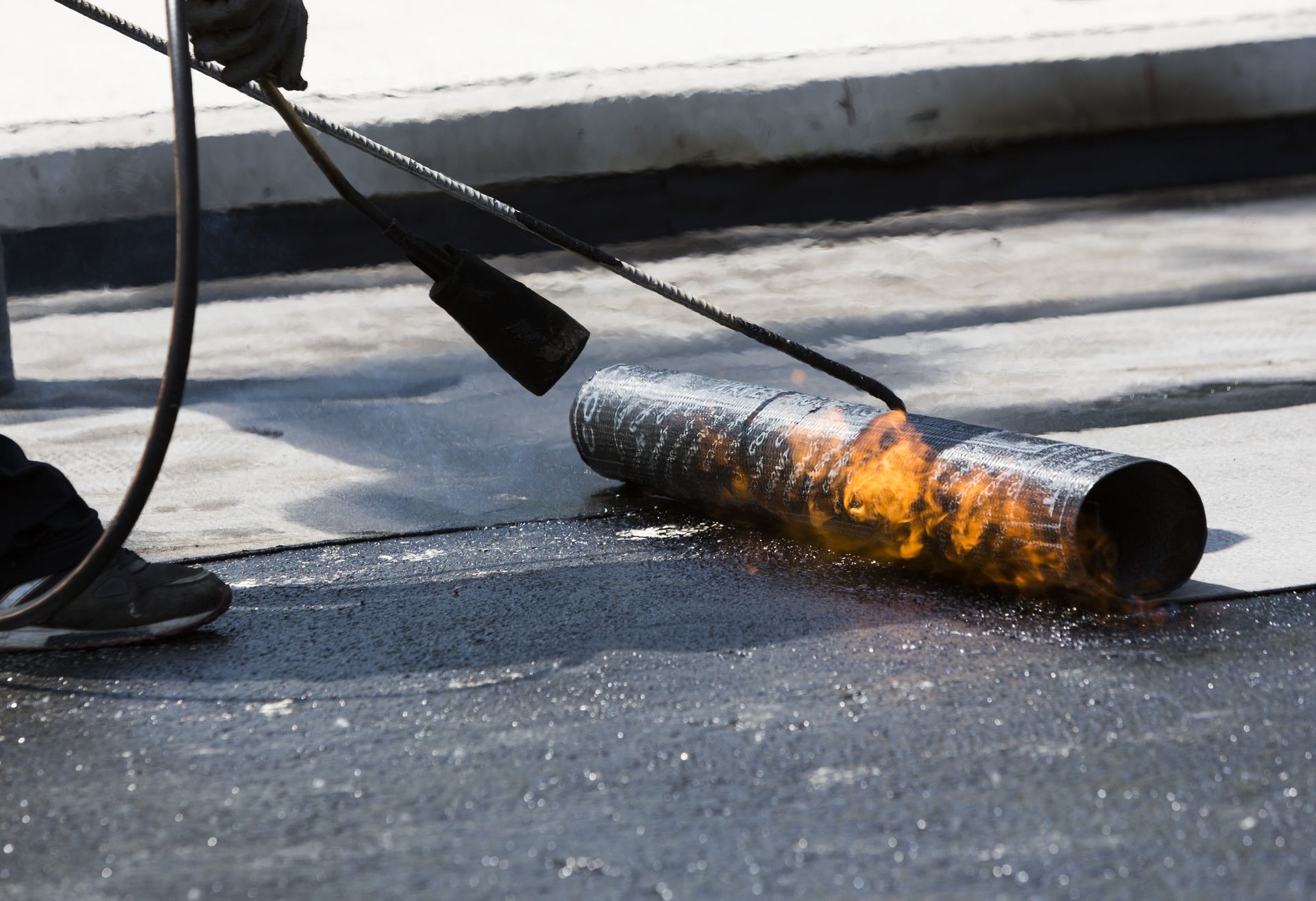 Person using a torch to seal roofing material on a flat roof.