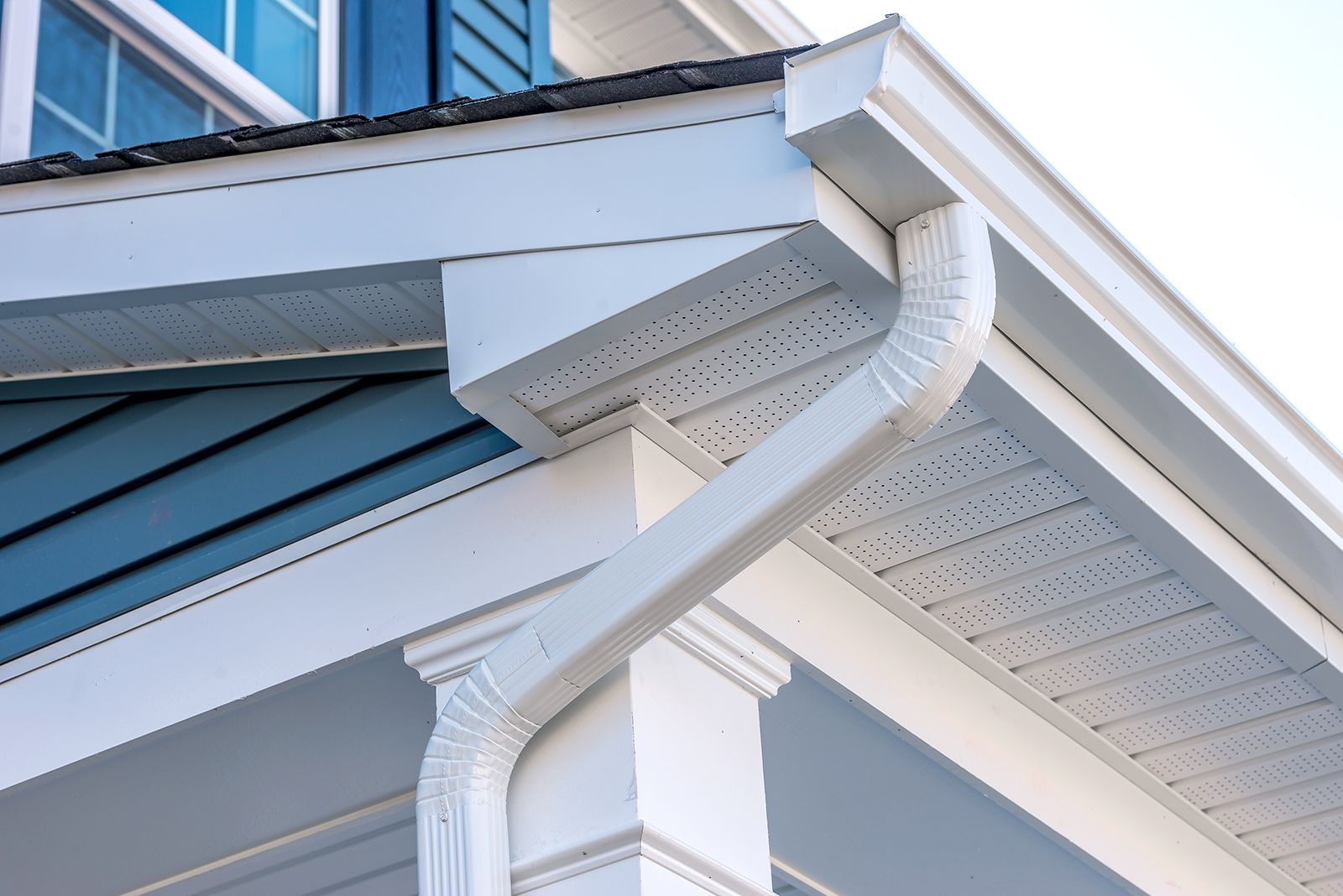 White gutter system on a light blue house, with a corner downspout.