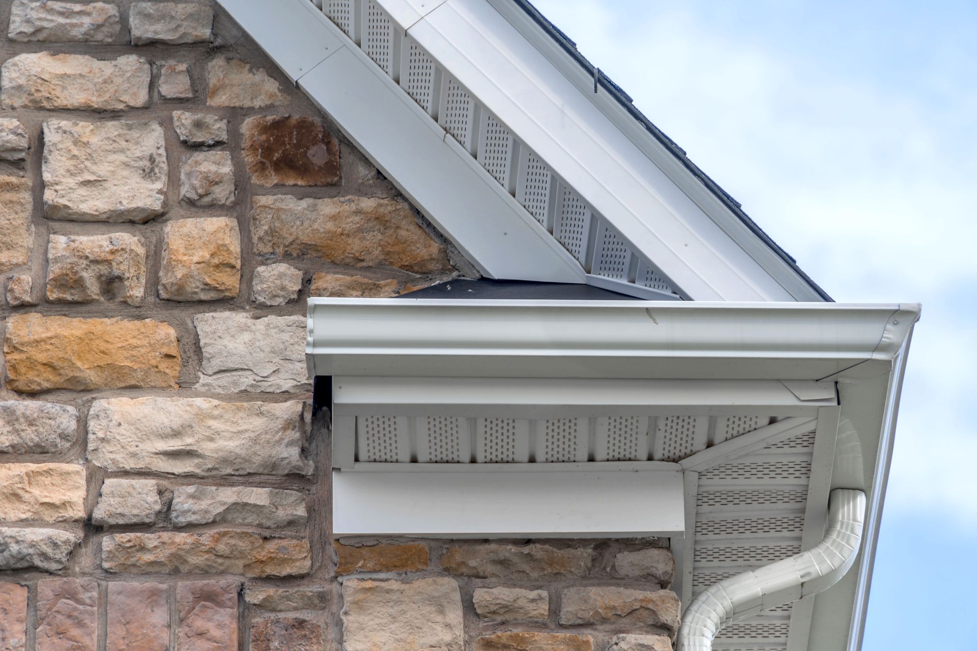 Corner of a stone brick house with white gutters and a section of roof.