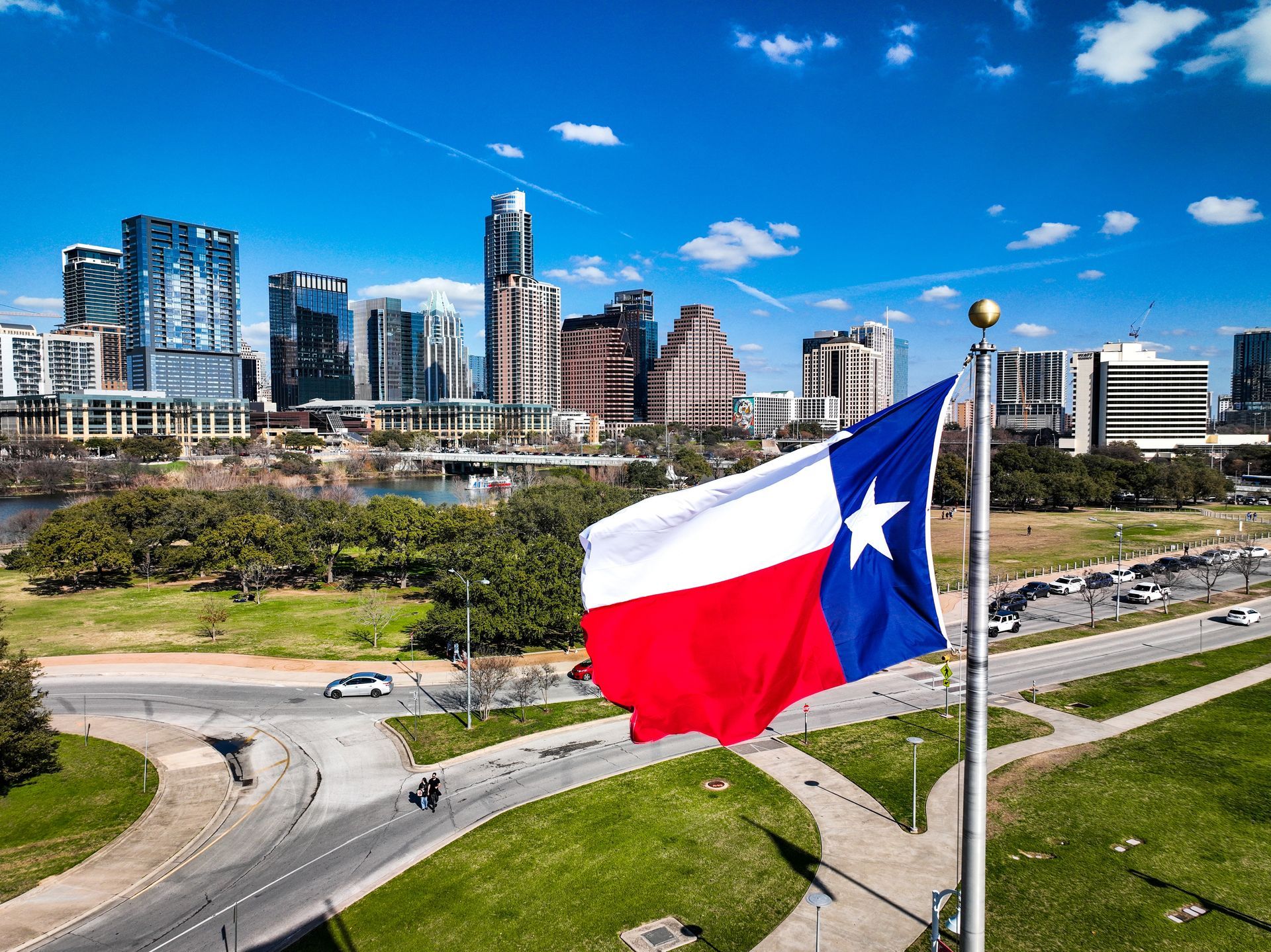 Texas state flag waving in front of the Austin skyline on a sunny day.