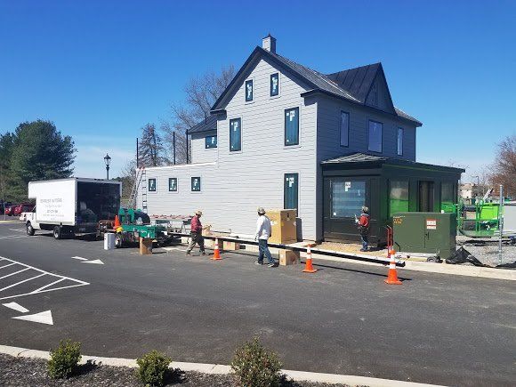Workers unloading boxes from a truck near a two-story gray building on a sunny day.