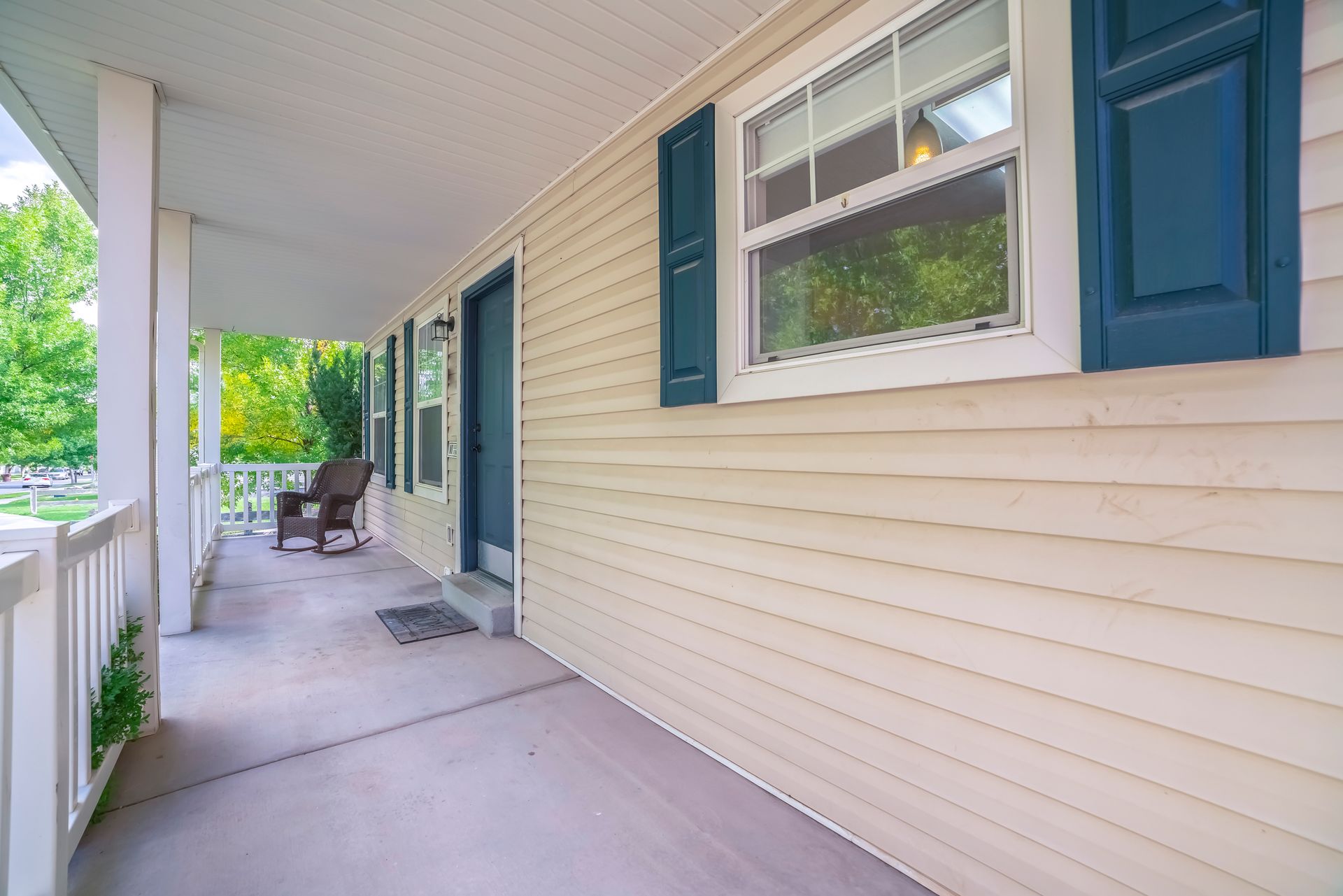 Covered porch of a house with beige siding, blue shutters, and a rocking chair.