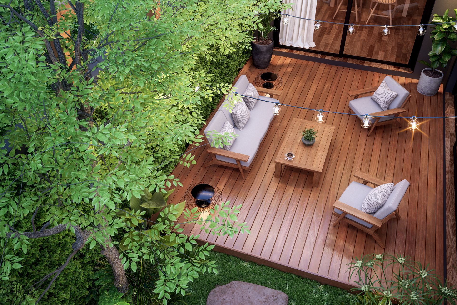 Overhead view of a wooden deck with outdoor furniture, surrounded by lush greenery, with string lights.