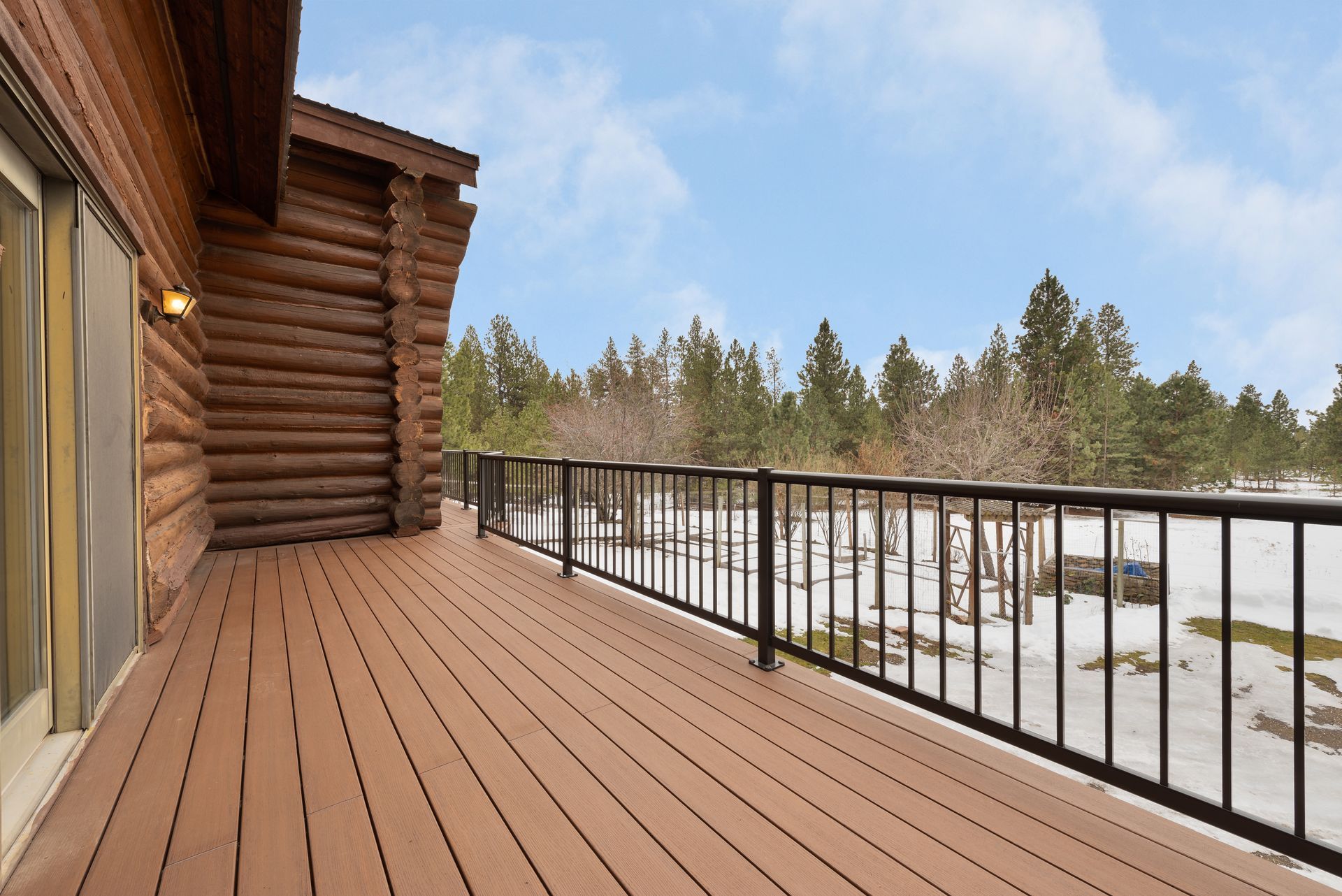 Wooden deck of a log cabin overlooking a snowy landscape with trees.
