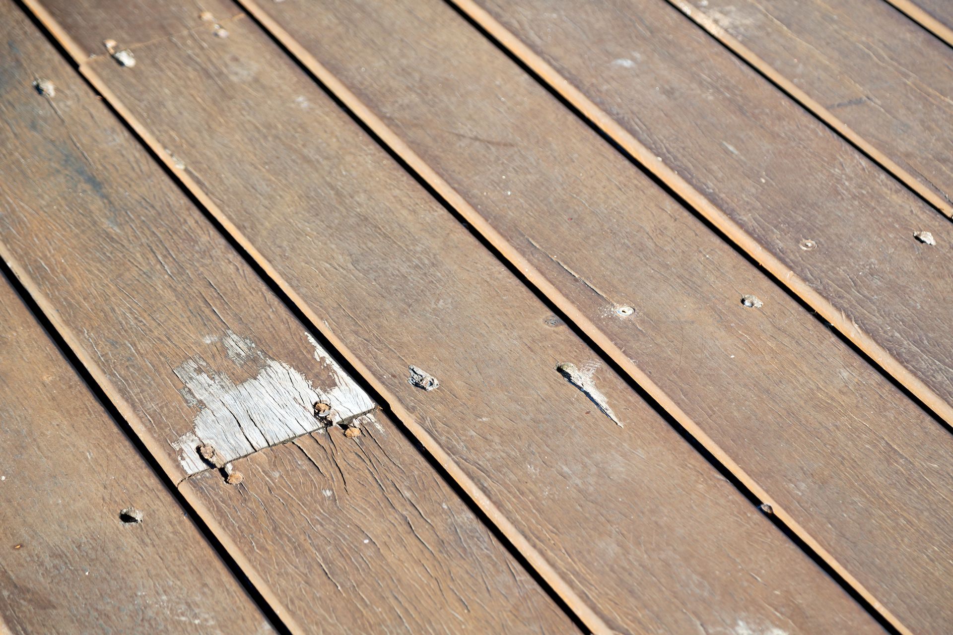 Wooden deck boards, angled, showing wear and tear, with some light-colored patches and small debris.
