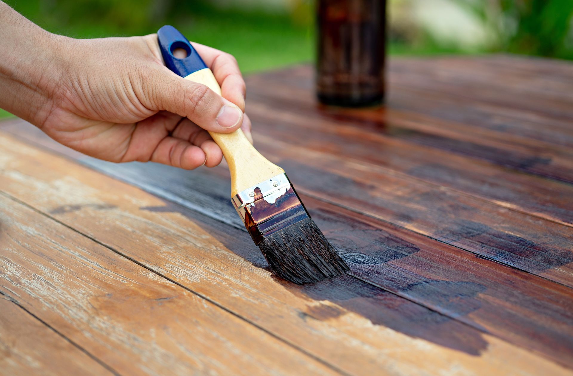 Hand staining a wooden tabletop with a brush; dark stain color.