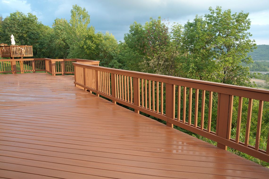 a wooden deck with a fence and trees in the background