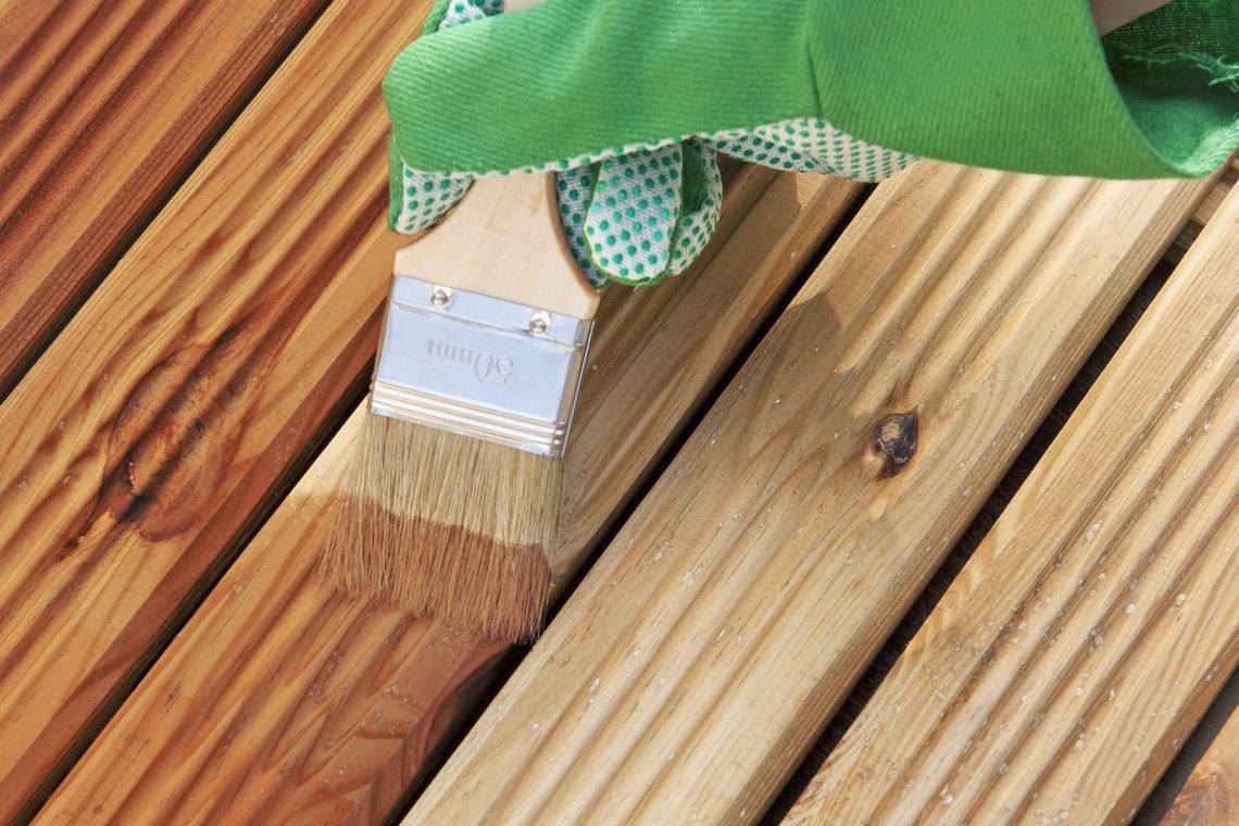 a person is painting a wooden deck with a brush .