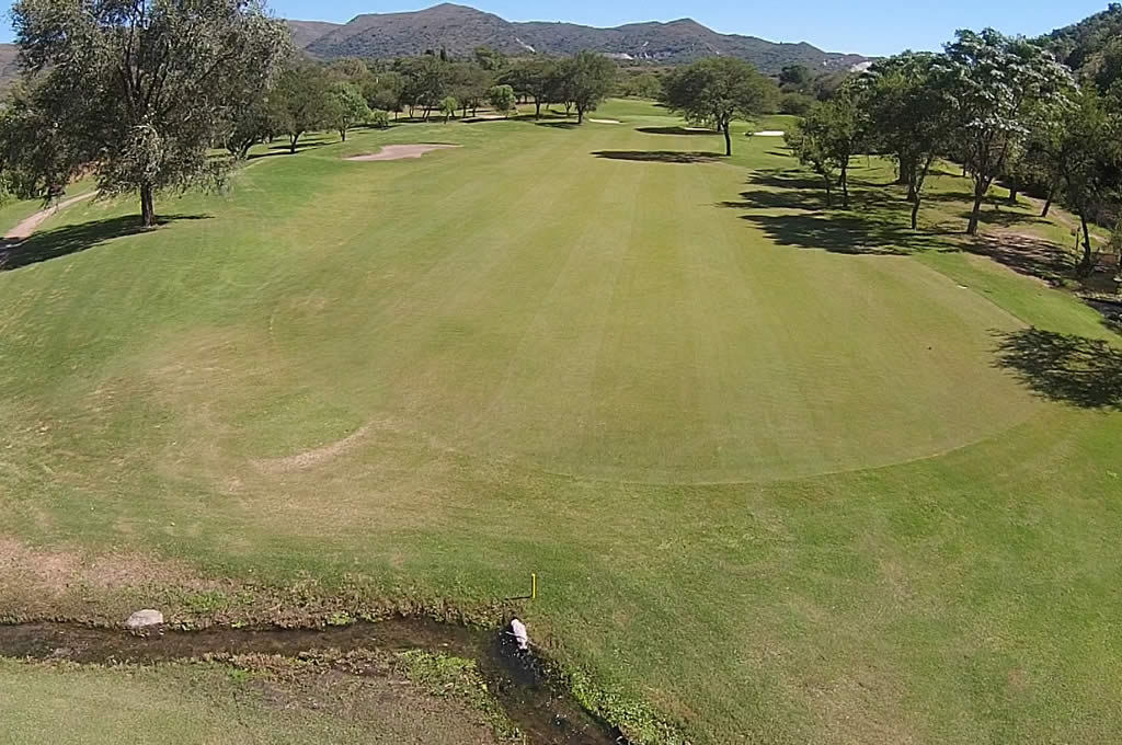 Una vista aérea de un campo de golf con árboles y montañas al fondo.