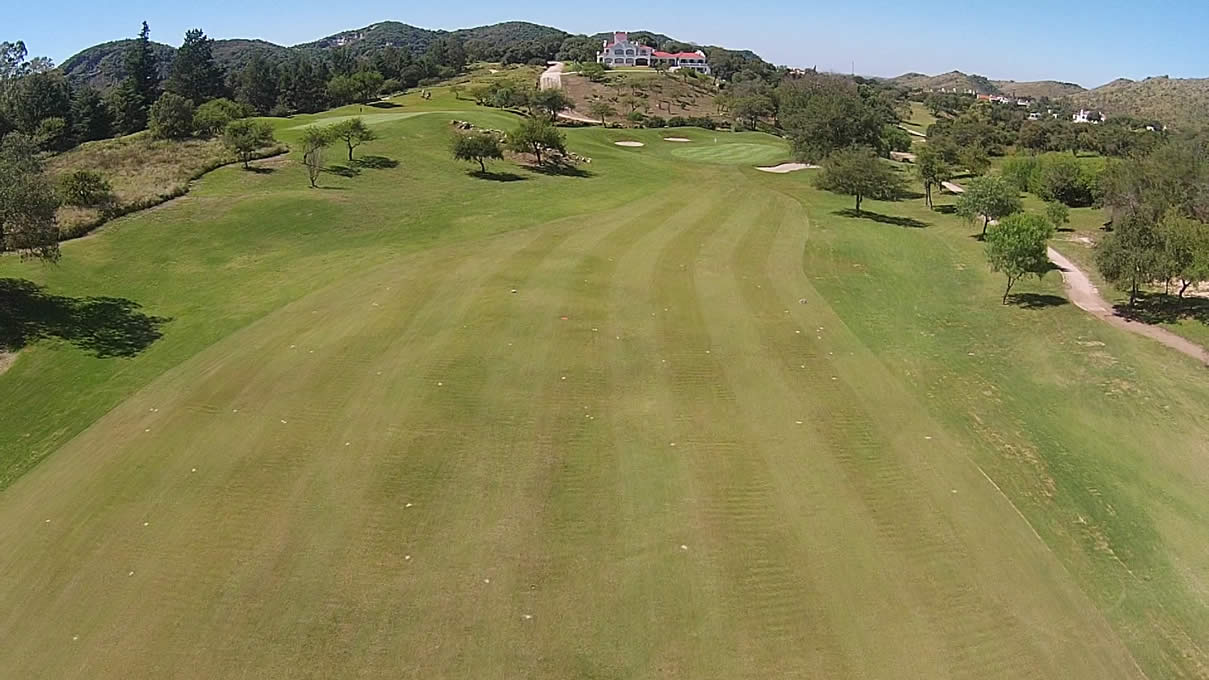 Una vista aérea de un campo de golf con una casa al fondo.
