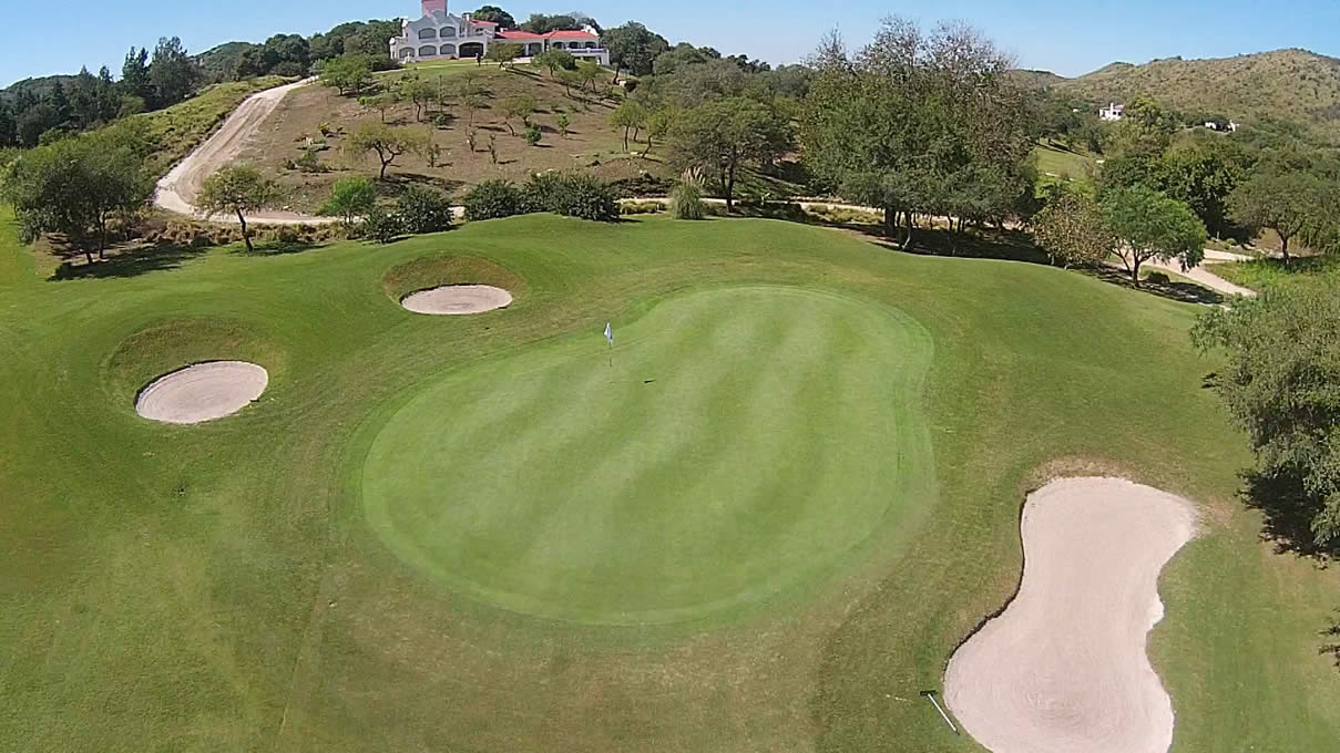 Una vista aérea de un campo de golf con una casa al fondo.