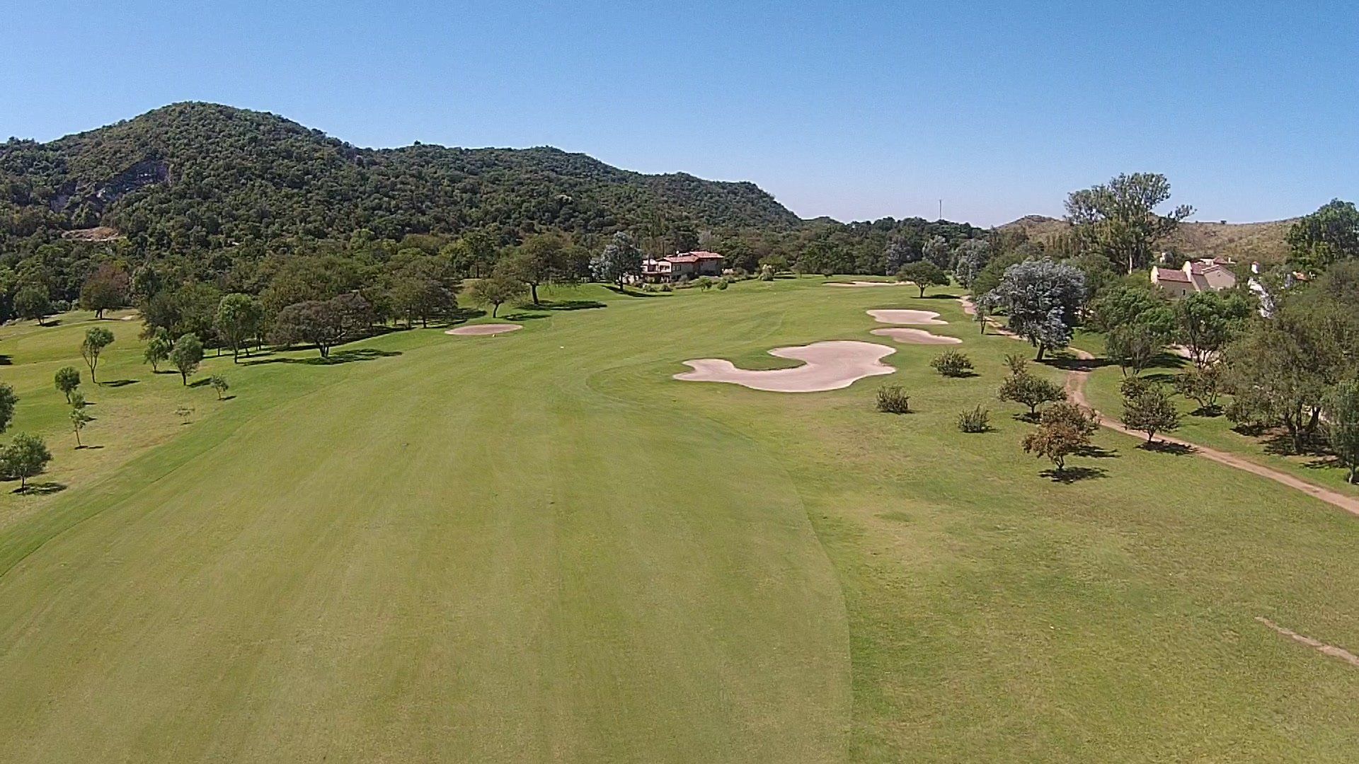 Una vista aérea de un campo de golf con árboles y montañas al fondo.
