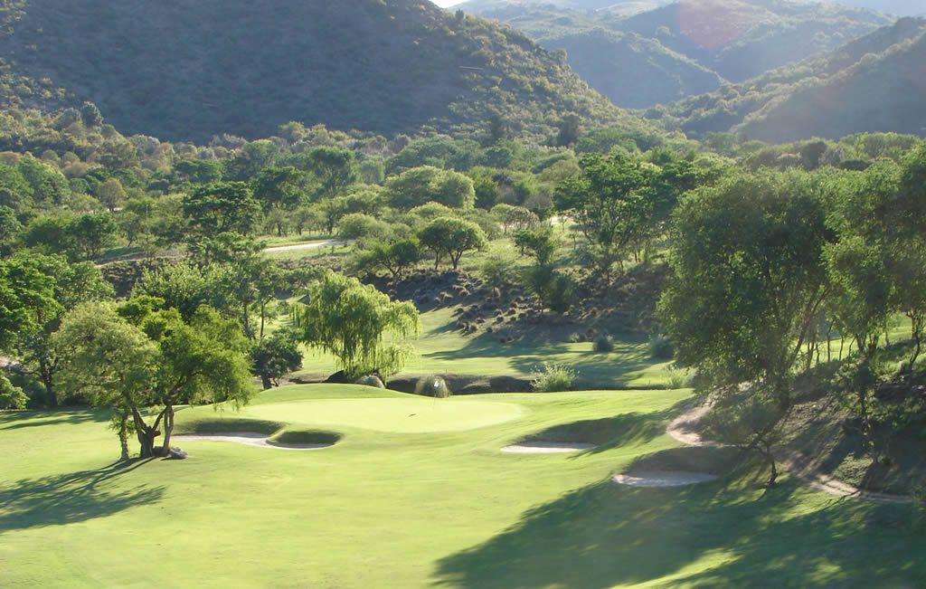 Un campo de golf con árboles y montañas al fondo.
