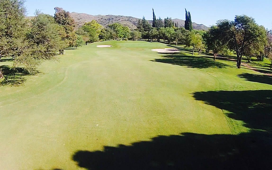 Una vista aérea de un campo de golf con árboles y montañas al fondo.