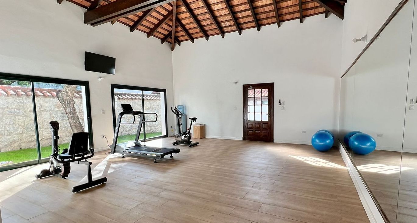 Un gimnasio con cinta de correr, pelotas de ejercicio y un gran espejo.