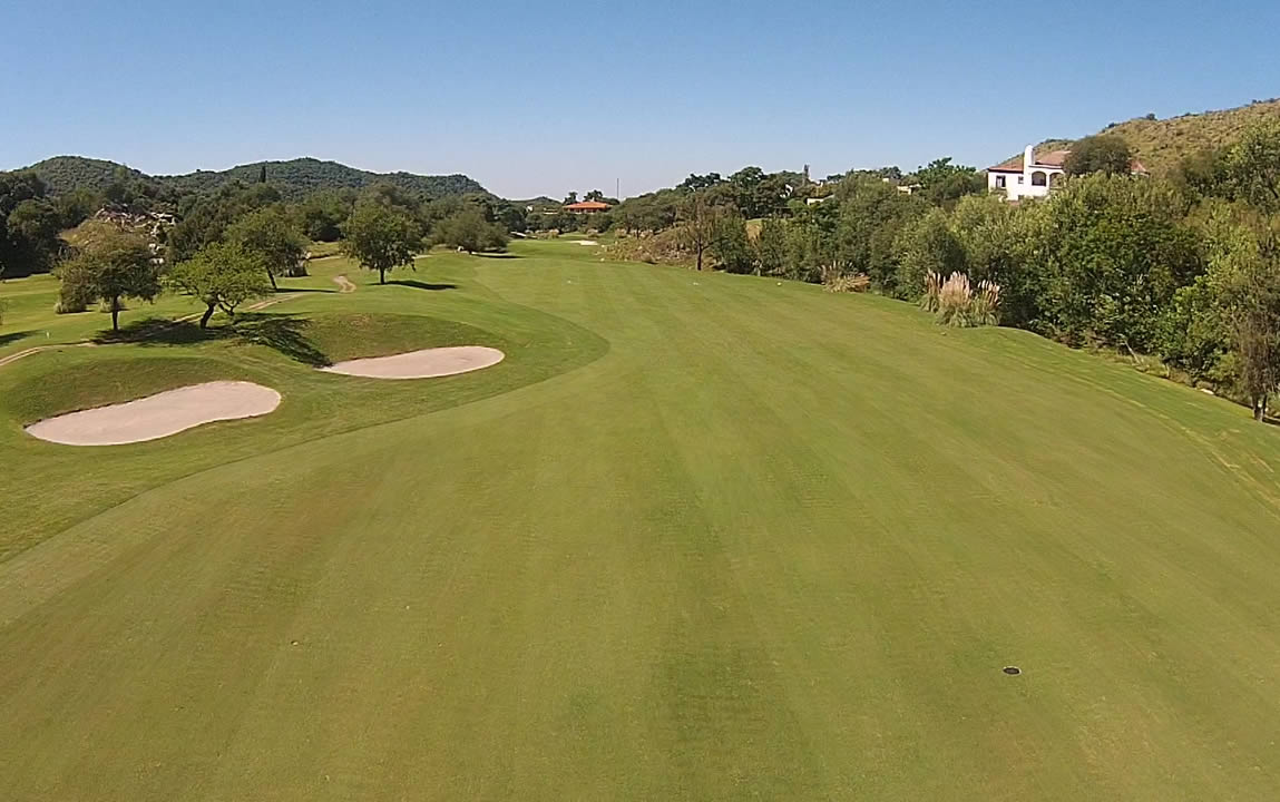Una vista aérea de un campo de golf con árboles y casas al fondo.