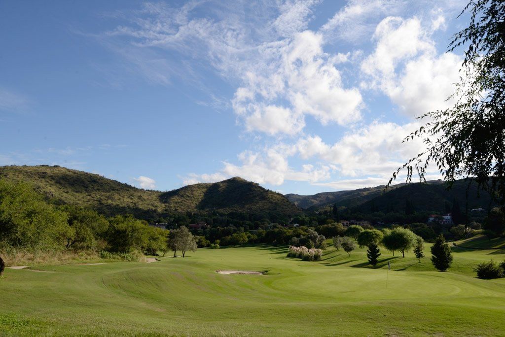 Un campo de golf con montañas al fondo en un día soleado