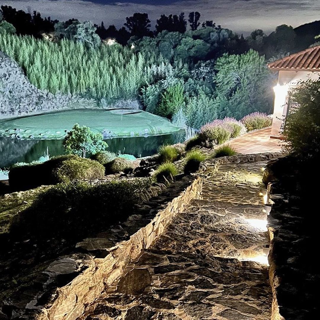 Un camino de piedra que conduce a una casa con un lago al fondo por la noche.