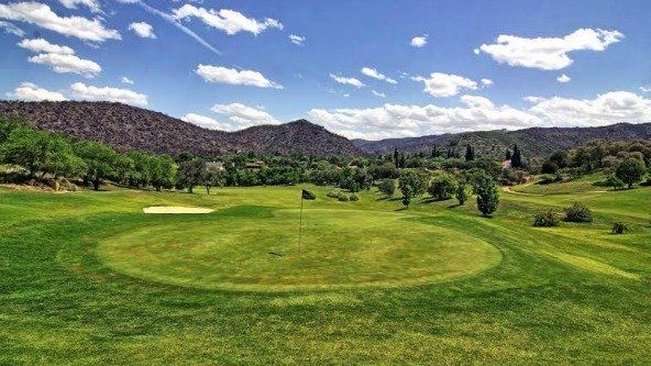 Un campo de golf con montañas al fondo en un día soleado.