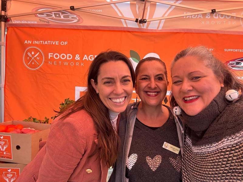 Three smiling people posing at a Food & Ag Network booth under an orange tent.