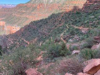 Hiking trail winds along a canyon wall; greenery and red rock formations.