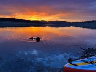 Sunset over a calm lake, paddleboard in the foreground. Orange sky reflecting in the water.
