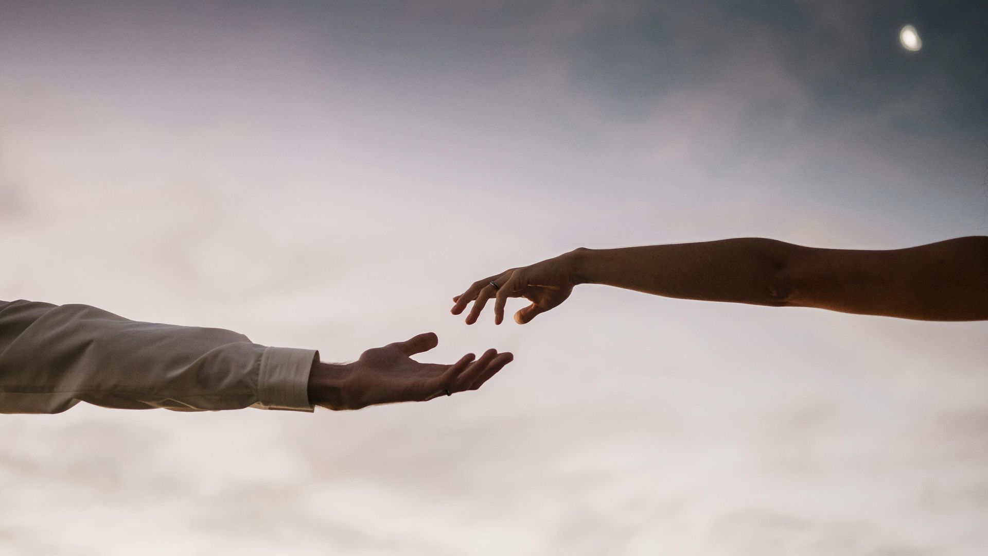 Two outstretched hands nearly touching against a cloudy sky, hinting at connection.