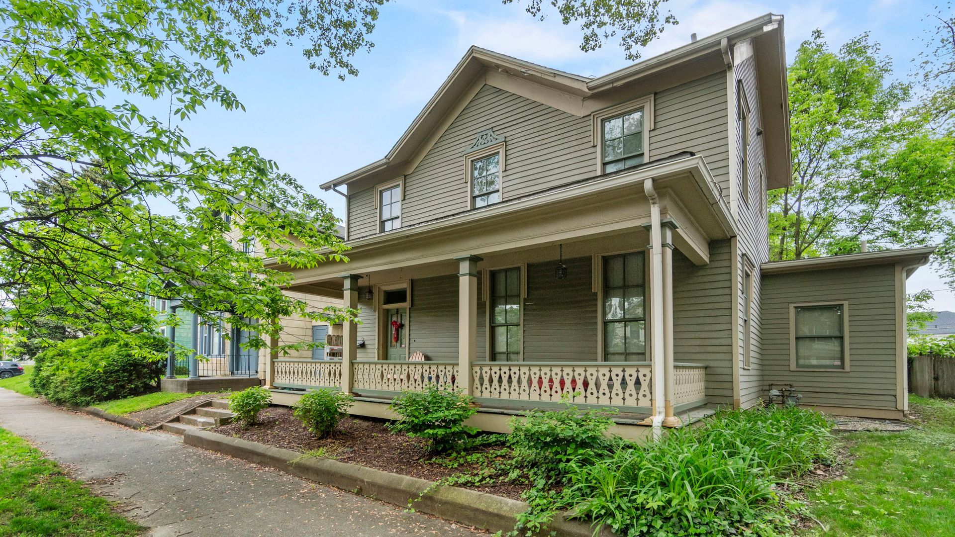 A large house with a porch and trees in the background.