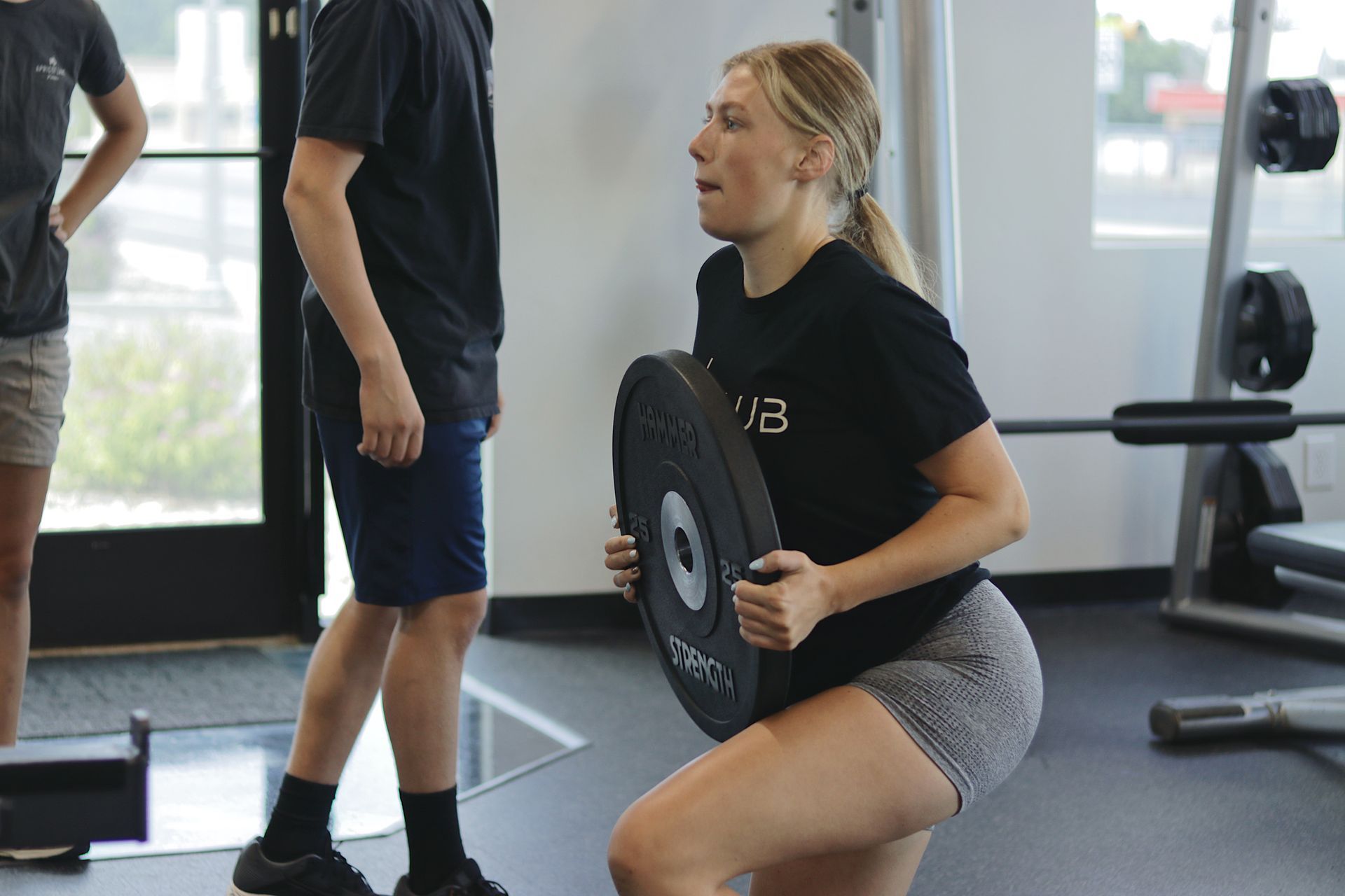 FitClub member performing squats with weight plate for strength training.