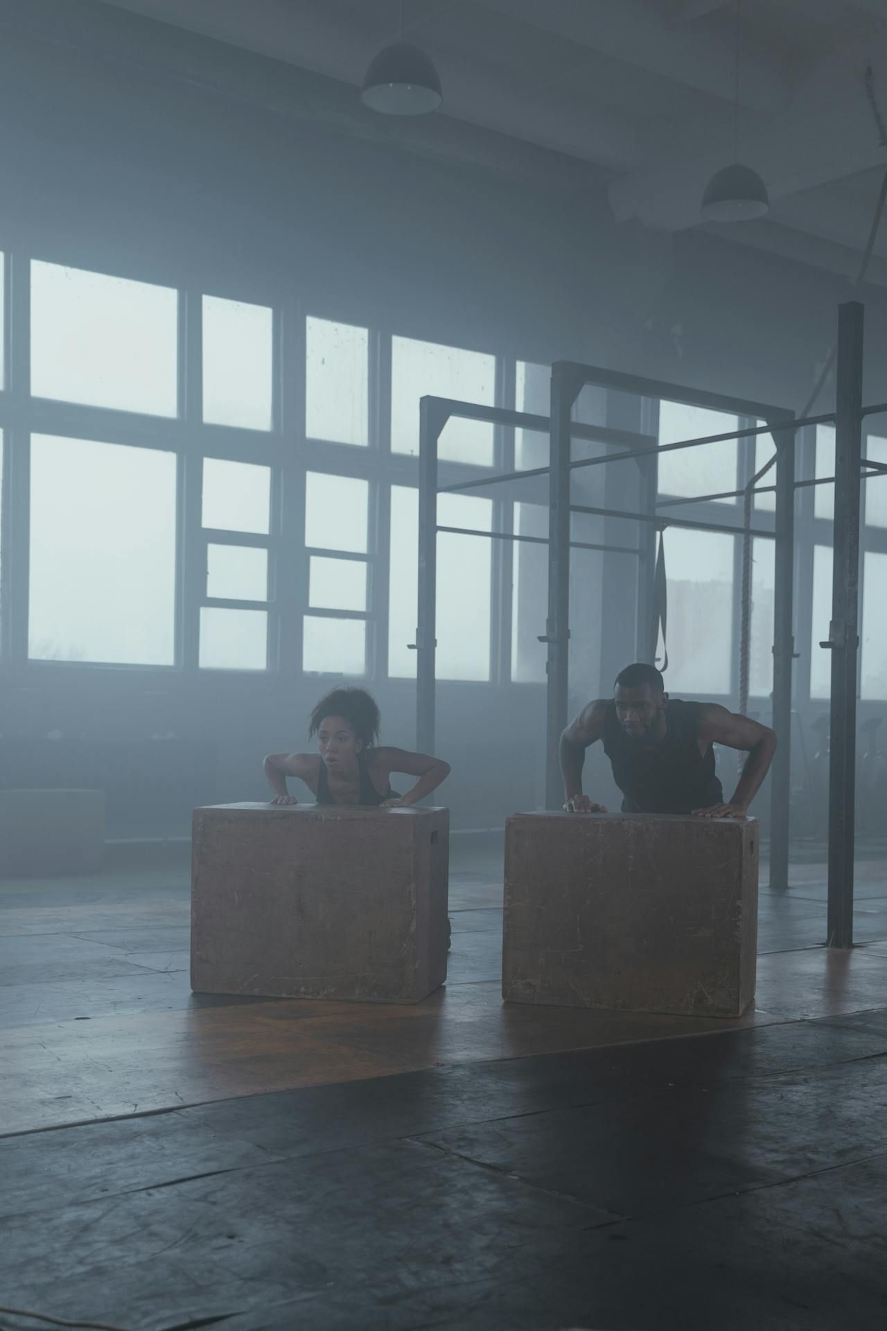 A man and a woman are doing push ups on wooden boxes in a gym.