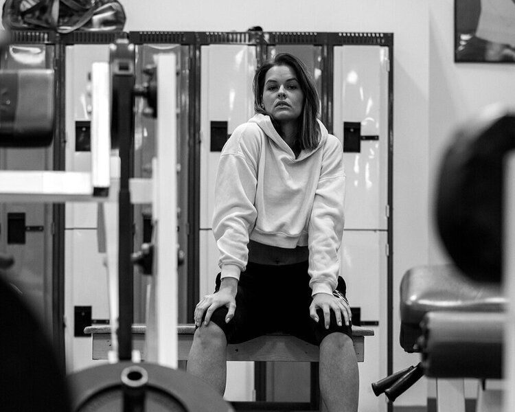 A woman is sitting on a bench in a gym.