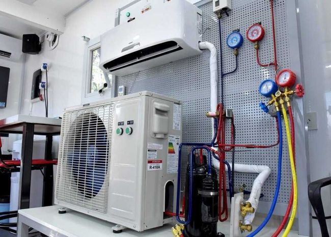Air conditioning unit set up for training, showing indoor and outdoor components with pressure gauges and tubing.